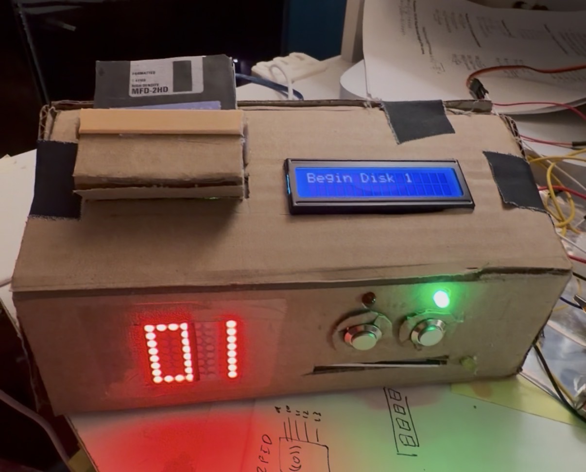 Disk 1 loading into the machine, which displays the disk number, a status LED, and a display reading "Begin Disk 1"