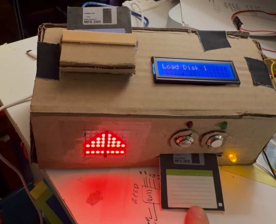 A prompt to load disk 1 on the box, which displays a load icon, a status LED, and a display reading "Load Disk 1"